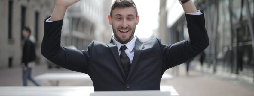 Retrato de homem em frente ao computador com mãos ao alto