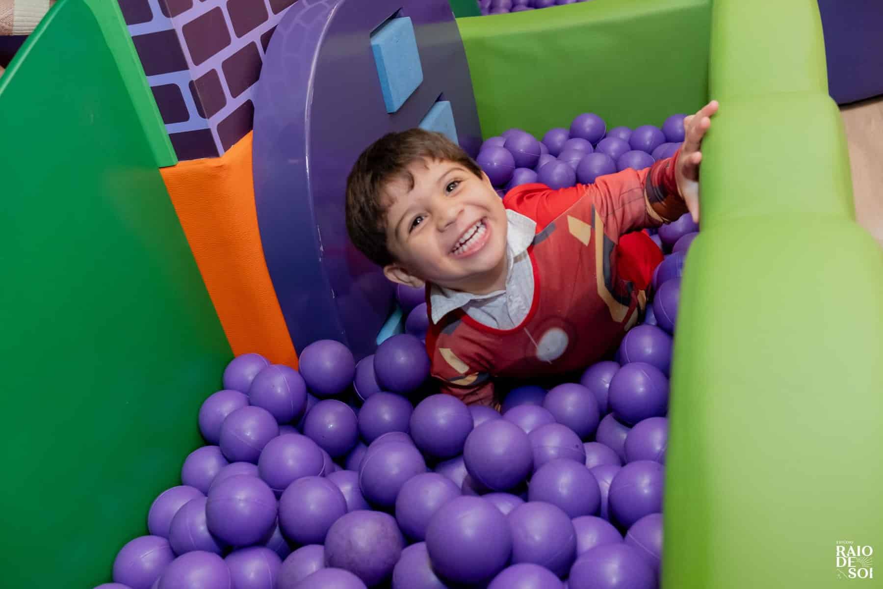 Criança sorrindo e brincando em piscina de bolinhas durante festa infantil.