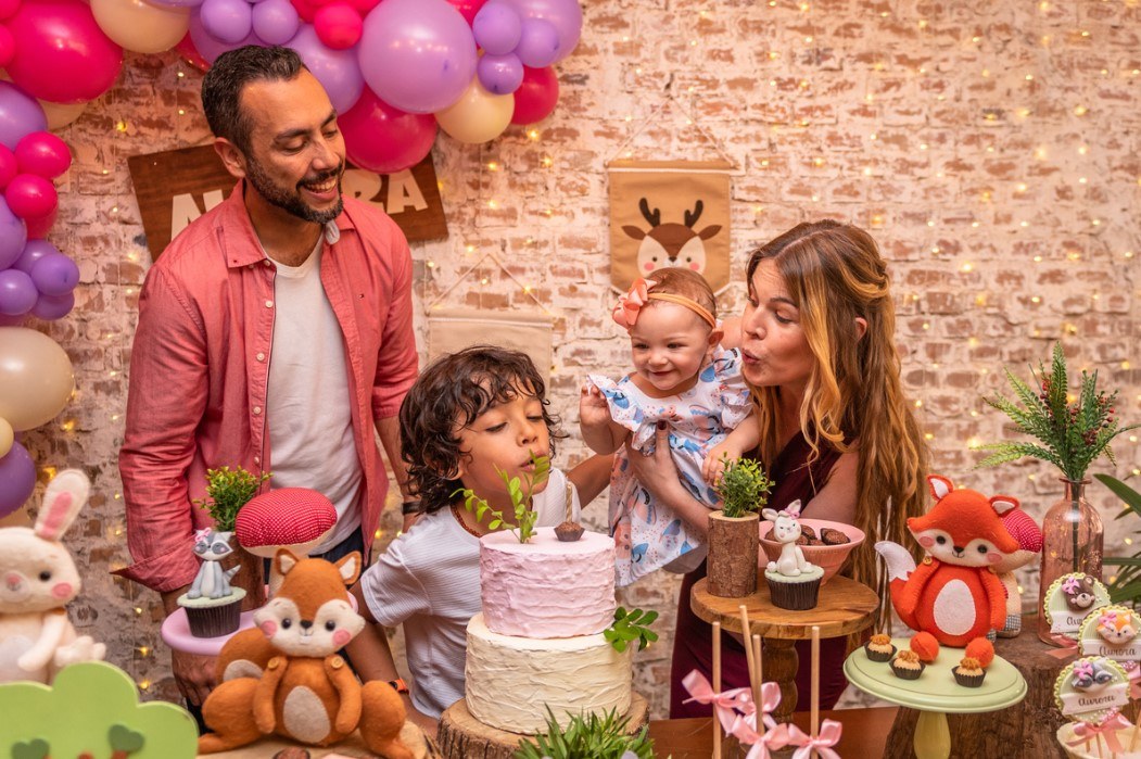 Família reunida diante do bolo em festa infantil com decoração de animais.